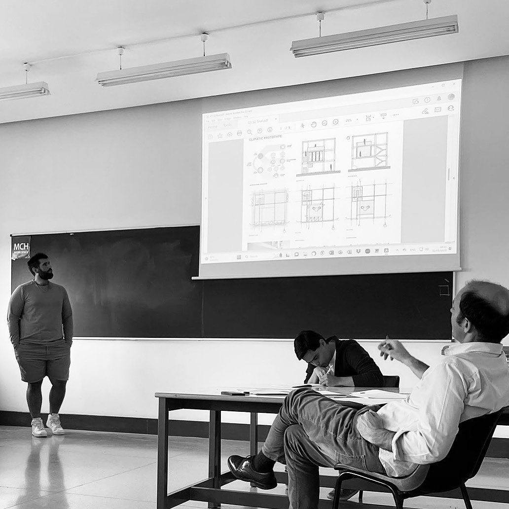 Presentation in a classroom with projected architectural drawings, and three people engaged in discussion.