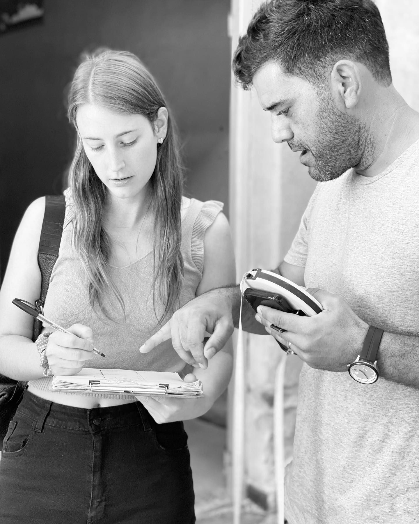 A person holding a clipboard while another person points at it, both engaged in a discussion.